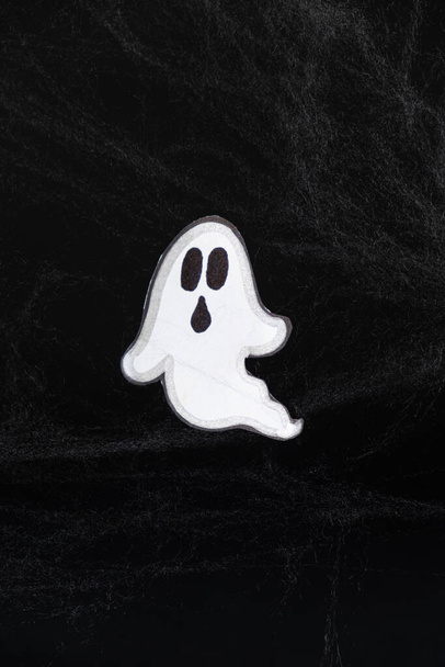 Ένα τρομακτικό λευκό φάντασμα πετά σε μαύρο φόντο με έναν ιστό, μια καρτ ποστάλ του Χάλογουιν. - Φωτογραφία, εικόνα