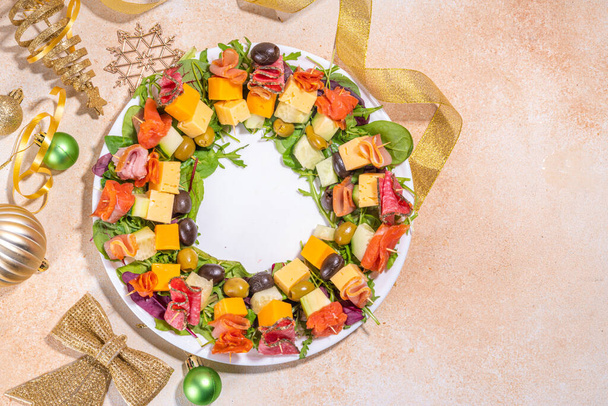 Christmas party dinner,  trendy layout appetizers. Charcuterie wreath made from sausage, meat, cheese, olives, greens on beige table background with gold Christmas decor top view copy space - Photo, Image