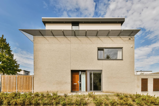una casa moderna con paredes de ladrillo y persianas de madera en la puerta principal, rodeada de plantas y arbustos verdes - Foto, imagen