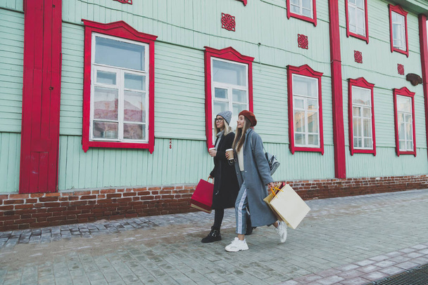 Jonge shopaholic vrienden vrouwen vrienden wandelen en dragen boodschappentassen in de straat lente of winter stad met gelukkig en glimlachend - aankoop en vrije tijd - Foto, afbeelding