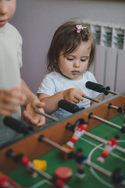 子供たちのテーブルサッカーを楽しんでいる赤ちゃんの女の子は、弟とエンターテイメントセンターを果たしています。趣味・レジャー - 写真・画像