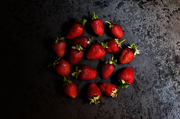 Ripe fresh red strawberries on dark background. Dark low key photo. Circle flat lay composition. - Фото, изображение