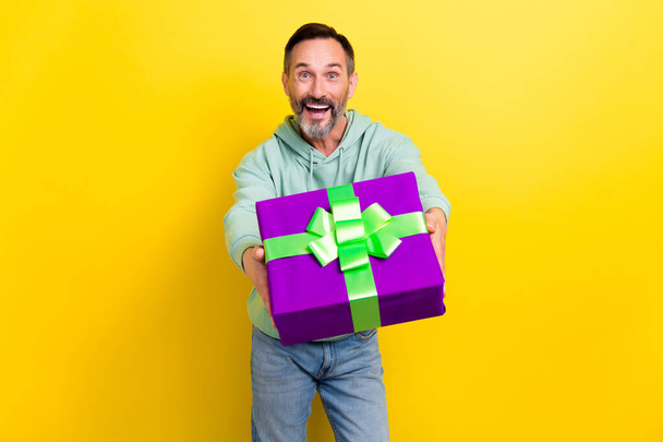 Photo of overjoyed man celebrate event give you present box good mood holiday occasion isolated on yellow color background. - Fotoğraf, Görsel