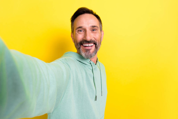 Portret dobrego nastroju zadowolony przyjemny przystojny mężczyzna ubrany zielony kaptur co selfie trzymać aparat odizolowany na żółtym tle kolor. - Zdjęcie, obraz