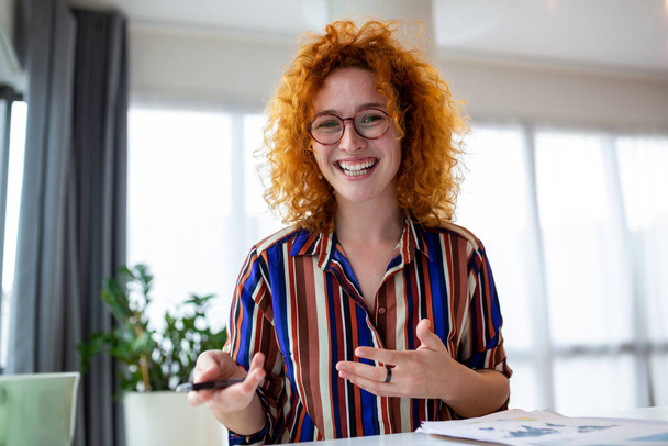 Aufnahme einer lächelnden Geschäftsfrau, die mit Laptop arbeitet, während sie in ein modernes Startup-Büro in die Kamera blickt. - Foto, Bild