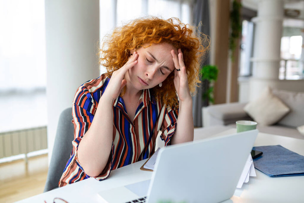 Wyczerpana bizneswoman z bólem głowy w biurze. Przepracowana bizneswoman doświadcza zmęczenia pracą podczas siedzenia przed laptopem. - Zdjęcie, obraz