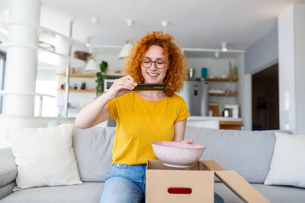 Young satisfied happy woman shopaholic customer sit on sofa unpack parcel delivery box, online shopping shipment concept. taking photos of product to post on social media - Fotoğraf, Görsel