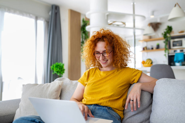 Femme assise avec ordinateur sur canapé, étudiant à la maison, e-learning et concept de travail indépendant à distance - Photo, image