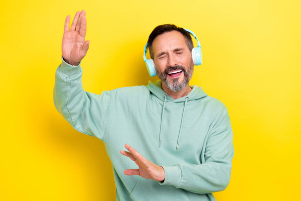 Портрет задоволеного чоловіка, одягненого в зелений светр слухати улюблені музичні плейлист танцює весело ізольовано на жовтому кольорі
. - Фото, зображення