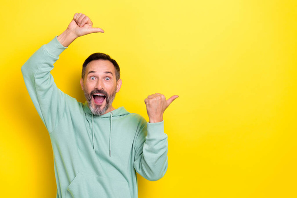 Portrait of impressed astonished positive man dressed green hoodie directing empty space open mouth isolated on yellow color background. - Фото, изображение
