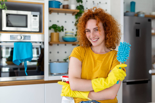 Молодая женщина выполняет домашнюю работу, держа в руках инструменты для уборки. Женщина в резиновых защитных жёлтых перчатках, держит тряпку и моющее средство для бутылок. Никогда не поздно прибраться. - Фото, изображение