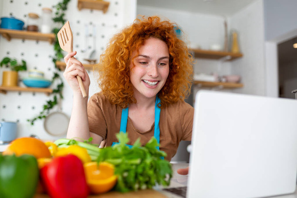 Młoda kobieta uczy się gotować, ogląda receptury wideo na laptopie w kuchni i gotować danie. Gotowanie w domu koncepcja - Zdjęcie, obraz