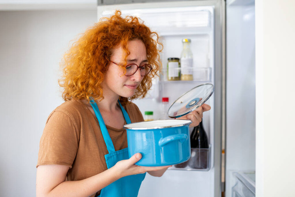 Bad Food In Fridge, young woman in holding her nose because of bad smell from food in refrigerator at home - 写真・画像