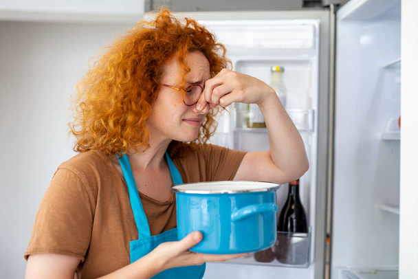Bad Food In Fridge, young woman in holding her nose because of bad smell from food in refrigerator at home - Valokuva, kuva