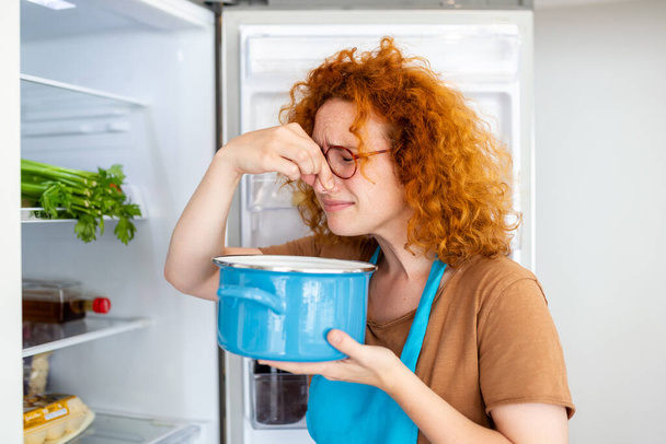 Bad Food In Fridge, young woman in holding her nose because of bad smell from food in refrigerator at home - Fotoğraf, Görsel