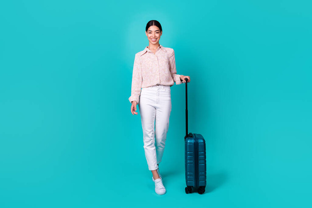 Full body photo of cheerful pretty malaysian lady walk carry suitcase isolated on vivid teal color background. - Φωτογραφία, εικόνα