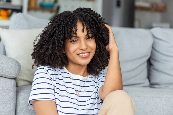 Portrait of a beautiful woman smiling at home. African woman in casual looking at camera with copy space. Cheerful mixed race girl relaxing at home with big laugh. - Zdjęcie, obraz