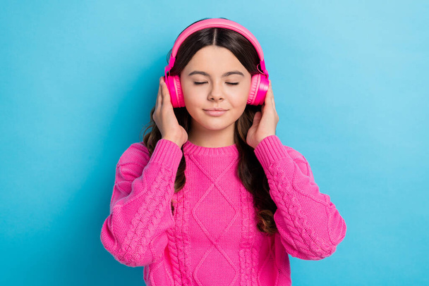 Photo of satisfied teen brown curly hair schoolgirl wear her new pink wireless earphones enjoy new rihanna album isolated on blue color background. - Фото, изображение