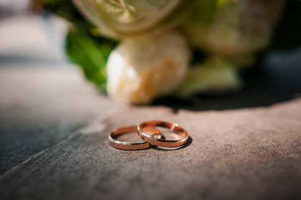 Arany jegygyűrűk, a háttérben a menyasszony csokor sokszínű virágok. - Fotó, kép