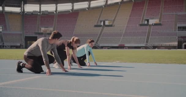 Három fiatal készül versenyezni a futópályán egy üres stadionban - Felvétel, videó