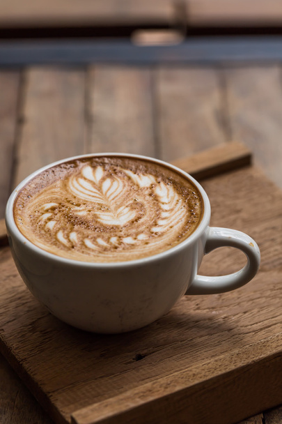 Cup of hot latte art coffee on wooden table - Fotó, kép