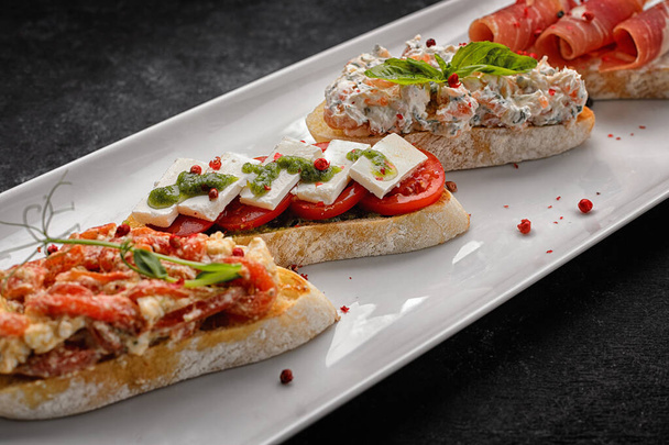 Bruschetta with homon, vegetables and cheese on a plate, on a gray concrete background - Photo, image