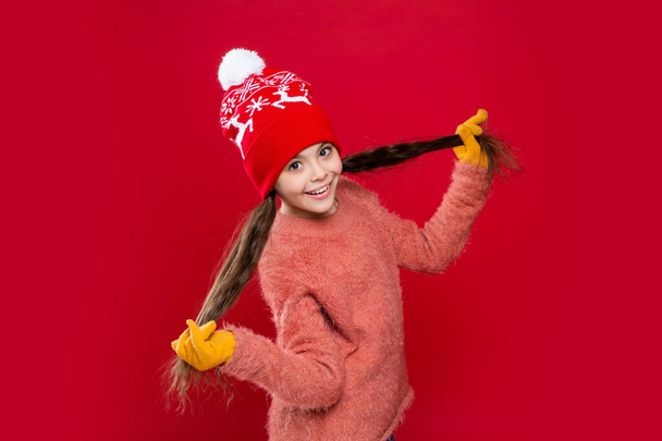 winter fashion for teen child having fun. hat knitwear. teen child model in hat. teen child in hat isolated on red background. teen child wear sweater and hat in studio. - Φωτογραφία, εικόνα