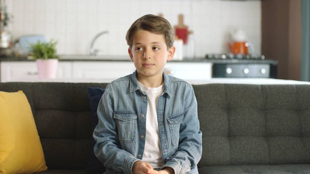 Retrato de un chico aburrido y triste en casa. Niño aburrido solitario sentado solo en el sofá en casa, sintiéndose deprimido y triste, mirando el espacio publicitario en blanco a la izquierda de la pantalla. - Foto, imagen