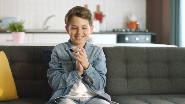 Kleiner Junge zeigt seine Freude auf dem heimischen Sofa in die Kamera. Der Junge ist sehr glücklich über die Nachricht, die er erhält. Konzept, Erfolg zu feiern. Lächelnde Emotionen, glückliche Kindheit. - Foto, Bild