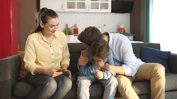 Young couple comforting their sad little son in the living room of their home.Portrait of parents caring for their children. The family hugs their children who are having problems at school. - Photo, Image