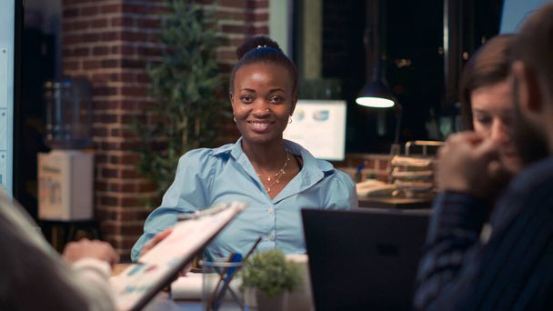 Femme d'affaires afro-américaine souriant portrait en réunion d'affaires, collègues parlant dans la salle de conférence, au ralenti. Divers collègues, femme regardant la caméra, plan moyen au ralenti. Coup de main. - Photo, image
