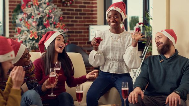 Veselí lidé cinkají sklenicemi vína a jsou nadšení z oslavy vánočních večírků v kanceláři s vánočními stromky a výzdobou. Různí kolegové slaví zimní prázdniny, dělají přípitek. - Fotografie, Obrázek