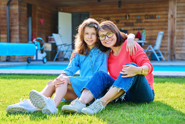 Portrait of happy mom and teenage daughter looking at camera. Smiling hugging mother and girl together in backyard near outdoor pool. Family, parent and child teenager, mothers day, lifestyle concept - Foto, immagini
