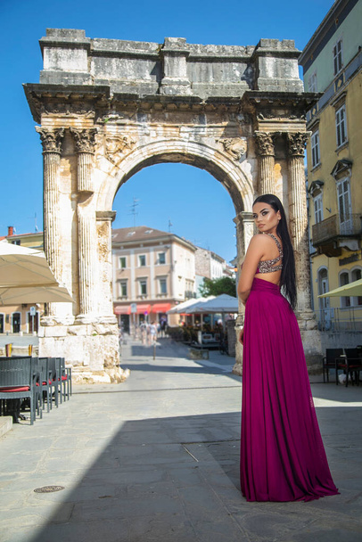 Uzun kırmızı elbiseli güzel siyah kadın şehrin eski bölümünde yürüyor. - Fotoğraf, Görsel