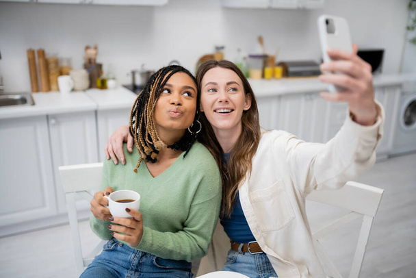陽気なレズビアン女性がアフリカ系アメリカ人の彼女とスマホで自撮り  - 写真・画像