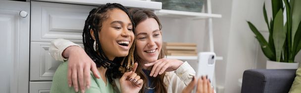 amazed african american lesbian woman using smartphone near smiling girlfriend, banner - Photo, Image