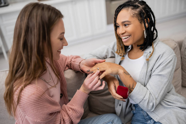 lesbian woman making proposal and wearing engagement ring on finger of happy african american girlfriend - Foto, Imagen