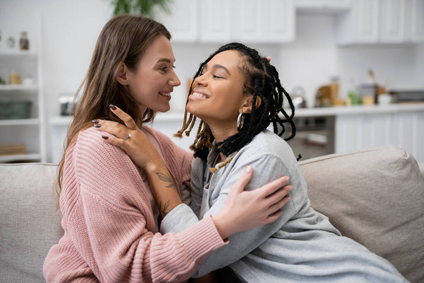 happy and tattooed african american lesbian woman with engagement ring hugging smiling girlfriend - Fotografie, Obrázek