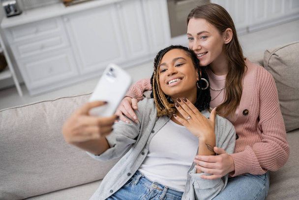 tattooed african american lesbian woman showing engagement ring while taking selfie with partner  - Foto, Imagen