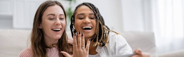 lesbian african american woman showing engagement ring near amazed girlfriend, banner  - 写真・画像