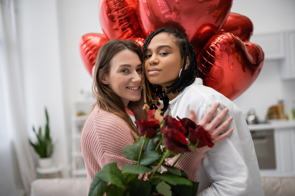 multiethnic lesbian women looking at camera near red roses and balloons on valentines day  - Zdjęcie, obraz