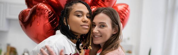 multiethnic lesbian women looking at camera near balloons on valentines day, banner  - Foto, Imagen