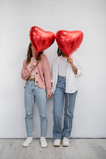 międzyrasowe lesbijki pokrywające twarze czerwonymi balonami w kształcie serca na szarości  - Zdjęcie, obraz