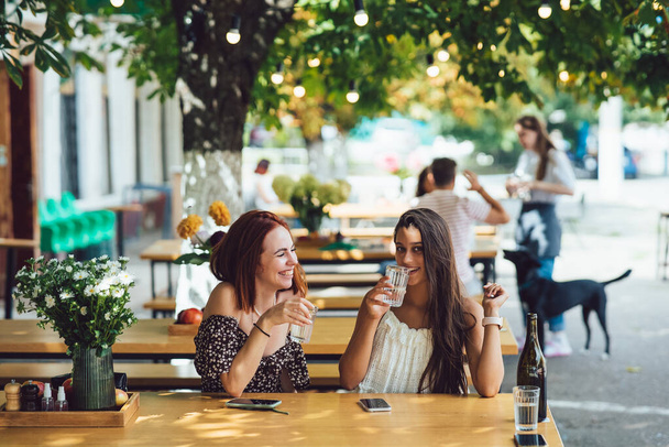 Two young beautiful women girlfriends talking in an outdoor cafe, gossiping, telling news together. Female friendship - Photo, Image