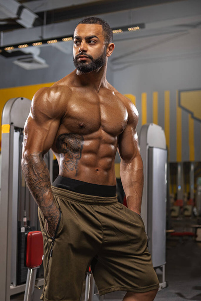 A strong athletic man with a naked torso poses at the gym. Image of a young adult man with a good physique in the gym. Strength and motivation. - Valokuva, kuva