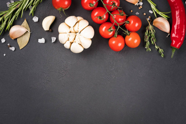 Variety of seasonings, herbs and vegetables over dark concrete background - food background with copy space for text. Garlic, tomatoes, chili pepper and rosemary - Fotografie, Obrázek