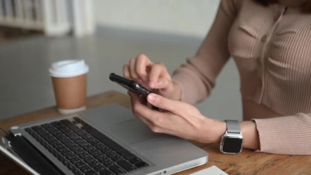 partial view of woman browsing smartphone and sitting at table with coffee and laptop  - Video
