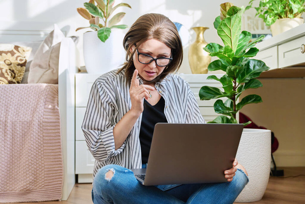 Mature woman using laptop for conference video call while sitting at home. Middle-aged female at virtual meeting with friends, colleagues, relatives, using video technology for work and leisure - Foto, imagen
