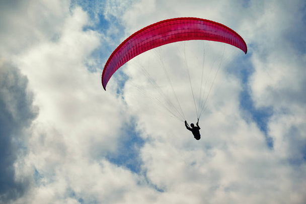 Paraglider in flight. Red paraglider in the cloudy sky - 写真・画像