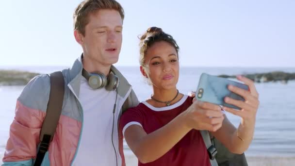 Interracial, selfie and couple with smartphone, beach and bonding together on vacation, loving and peace sign. Young man and Latino woman with phone, hand gesture and post for social media or holiday. - Footage, Video